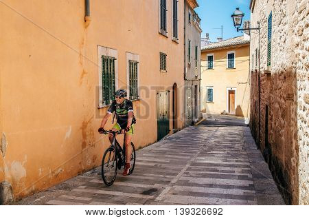 Alcudia Mallorca Spain - May 23 2015: Bicyclist rides along a narrow street of the historical town part of Alcudia with its traditional house and paving stone