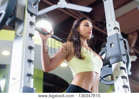 Fit woman doing squats with the barbell Smith machine in the gym