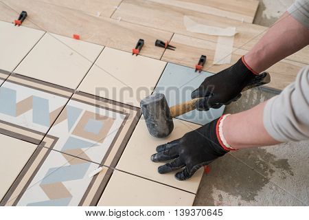 Laying colored ceramic tiles on the concrete floor in the living room of a city apartment. In working hands holding a hammer debugging.