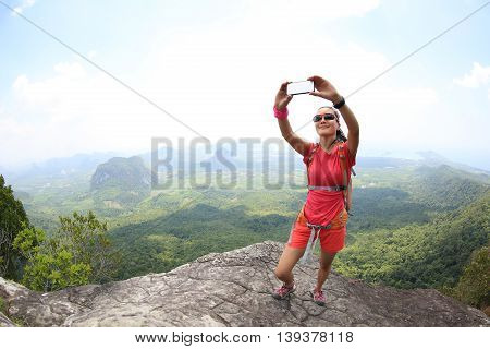 young woman hiker use smartphone taking self photo on seaside mountain top
