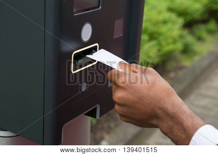 Close-up Of Person's Hand Inserting Ticket Into Parking Meter To Pay For Parking