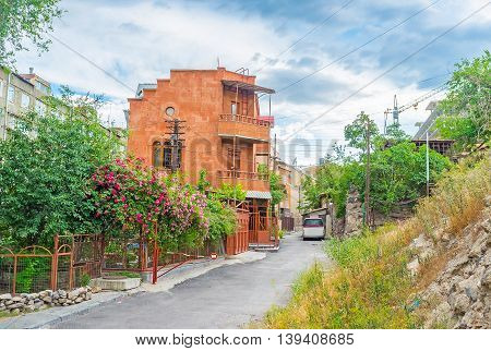 The red tuff cottage surrounded by the scenic garden with wild rose bushes in blossom Yerevan Armenia.
