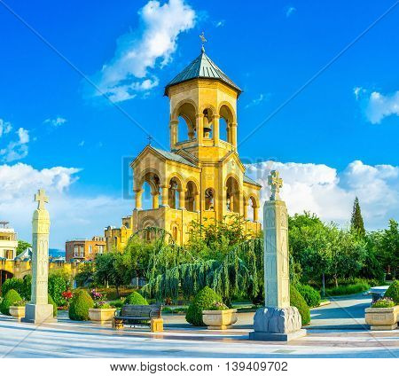 The high stone bell tower of Sameba (Trinity) Cathedral surrounded by lush green garden Tbilisi Georgia.