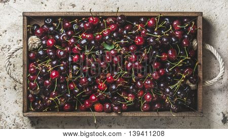 Ripe sweet cherries in rustic wooden tray over light concrete background, top view, horizontal composition