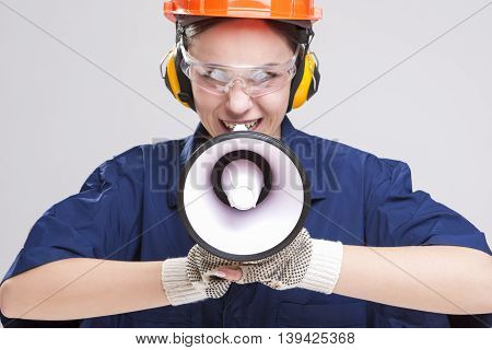 Expressive Caucasian Female Worker Posing with Megaphone and Wearing Hardhat for Protection. Horizontal Image Composition