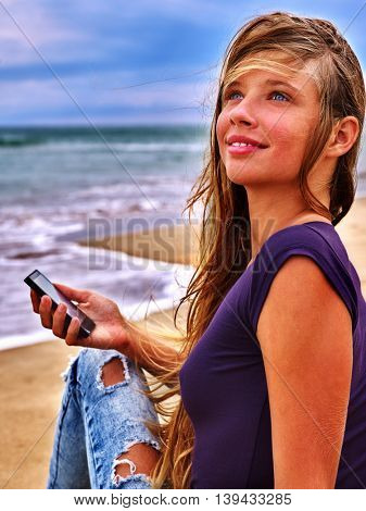 Girl with mobile phone sitting on sand near sea. First love of girl with phone sitting on sea beach