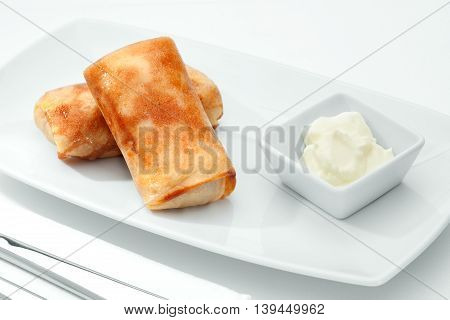 close up view of nice yummy crepes with sourcream on white