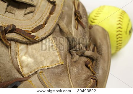 Softball glove in focus with blank tag and yellow softball in background