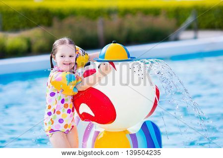 Happy laughing little girl playing in outdoor swimming pool on a hot summer day. Kids learn to swim with colorful floaties.