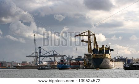 Loading and Unloading Shipping Containers in the Port of Rotterdam. Cranes and cargo containers alongside container ships moored at commercial dock.
