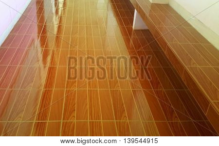 hallway floor with pink walls reflecting in the shiny brown tiles, matching brown-tiled bench along the wall on the right, white pillar post passing through the bench at top of photo.