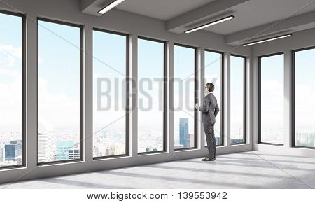 Man in empty office room looking at big city through large window. Concept of thoughtfullness. 3D render.