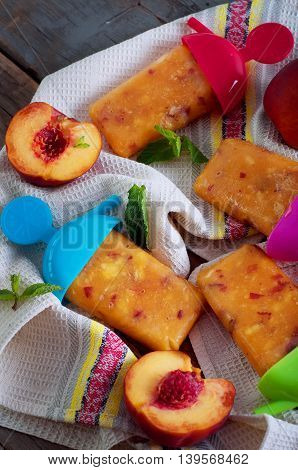 Peach ice lollies with colores sticks on a kitchen napkin with mint leaves