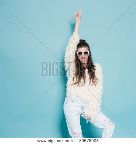 studio portrait of cheerful fashion hipster girl going crazy making funny face and dancing. Blue color background.