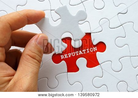 Hand holding a piece of white puzzle with word REPUTATION