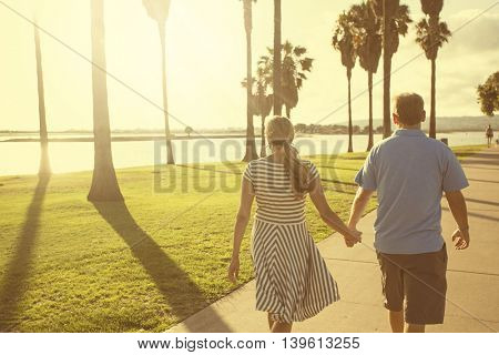 Middle aged couple walking together holding hands along the beach boardwalk. Abstract image of Building relationships and marital bonds. Early evening sunset and warm summer tone