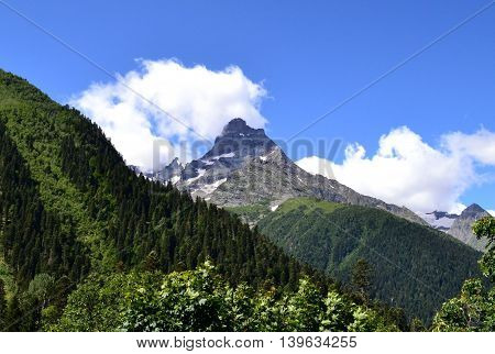 Mountain peaks and forests on the background of clouds and sky. Dombay - a mountainous area in Karachay-Cherkessia in the basin of the Teberda in the North Caucasus (Russia). Photo taken on: July 26 Friday 2013