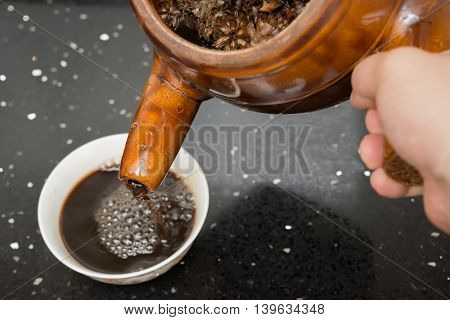 pouring herbal tea from an enamel pot with herb to a bowl