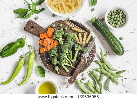 Raw ingredients for cooking vegetarian lunch - dry pasta fresh broccoli zucchini green peas and beans carrots olive oil. On a light background top view