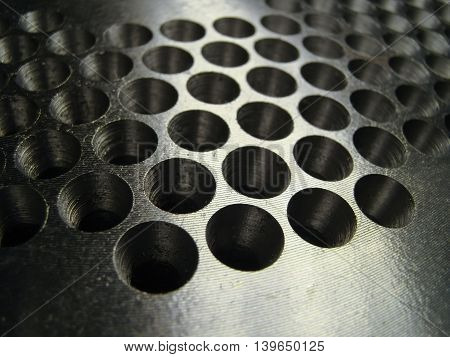 Many holes drilled in a shiny metal plate for matrix extruder detail.