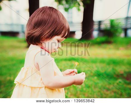 Little Baby Girl Portrait in profile outdoor. Cute Child over nature background. Adorable one year old baby with flower in hands