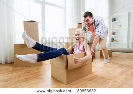 home, people, moving and real estate concept - happy couple having fun and riding in cardboard boxes at new home