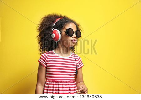 Afro-American little girl with headphones listening to music on yellow background