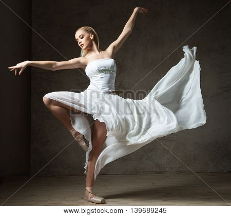 Elegant ballerina in white dancing with arms outstretched and flying skirt in studio