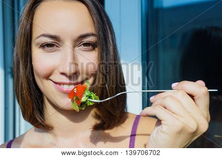 A girl holding a fork with vegetables smiling young girl sunny day with fresh vegetables tomatoes and cucumbers leaf lettuce. Useful food vegetarian salad.