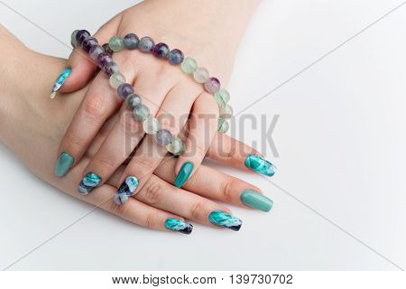 Closeup of woman nails with creative purple and green manicure. Fluorinit print. Natural stone beads. Copy space.