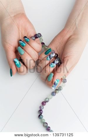 Closeup of woman nails with creative purple and green manicure. Fluorinit print. Natural stone beads. Copy space.