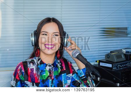 Beautiful girl in headphones with a microphone on the radio in the studio