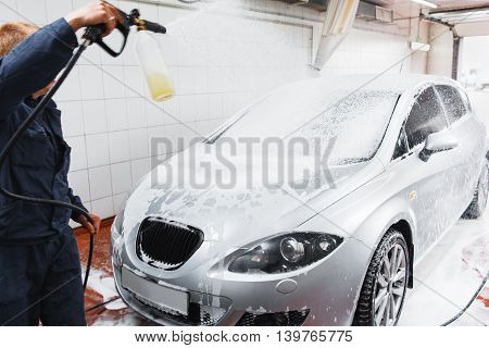 Serviceman in carwash washing car with hose. Handle automobile cleaning at special store, complex service