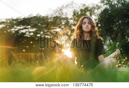 The women meditates on the grass at sunset
