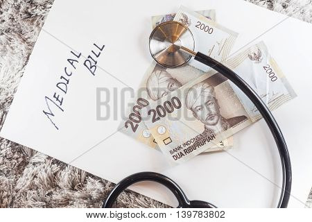 Stethoscope with wording of "Medical Bill" showing expensive healthcare or expensive medical bill with Indonesia Rupiah Bank Notes