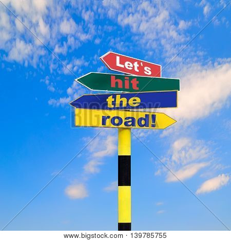 Sign post with four arrows of diffirent colors and directions and text - Let s hit the road on a blue sky background.