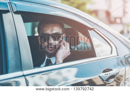 Businessman on the phone. Serious young businessman talking on the mobile phone while riding inside his car