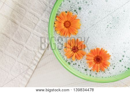 Soothing cleansing foam bath with calendula. Bright flowers, aromatic foam in green bowl, white towel background. Top view.