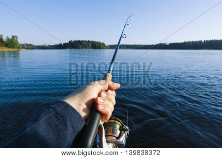 Fishing on a lake at sunset. Fishing rod with a reel in hand.