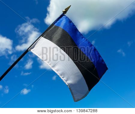 Close-up of the Estonian flag, symbol of freedom and representing one of the Baltic countries, held up against a blue sky with a few clouds for contrast.