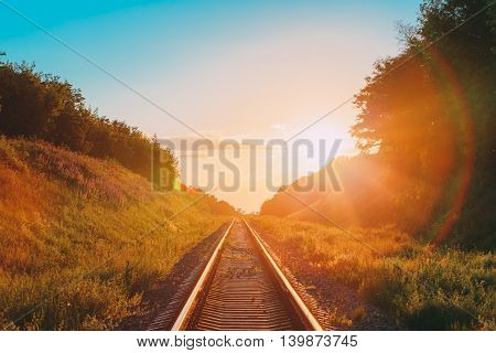 The Scenic Landscape With Railway Going Straight Ahead Through Summer Hilly Meadow To Sunset Or Sunrise In Sunlight. Lense Flare Effect.