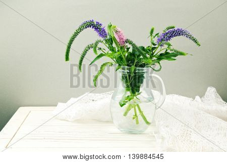 Flowers in glass jug on wooden table with lace textile