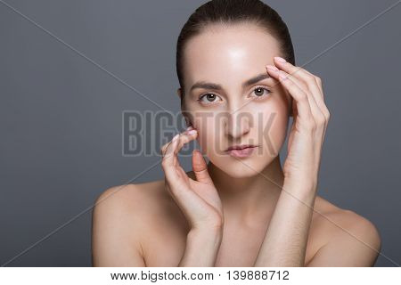 Beauty fashion vogue style face of caucasian brunette with elegant make-up blue eyes natural lips touching perfect skin. Close-up studio portrait isolated. Black background with grey spot. Toned.