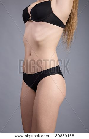 Close up photo of slim woman's body in black lingerie on gray background
