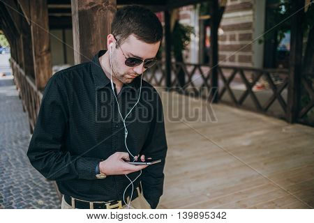 A guy in a nice town, walking, listening to music and taking pictures themselves on the phone