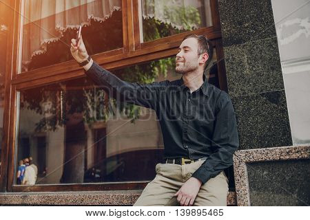 A guy in a nice town, walking, listening to music and taking pictures themselves on the phone