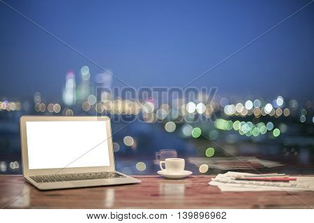 Front view of creative designer desktop with blank white laptop stationery items and coffee cup on blurry night city background. Mock up