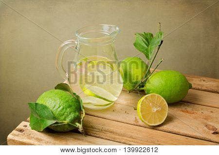 Lemons with leaves and water jug on wooden table