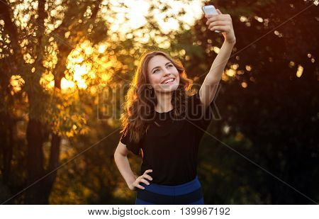Young Pretty Brunette Doing Selfie in Prak on Nature Background.