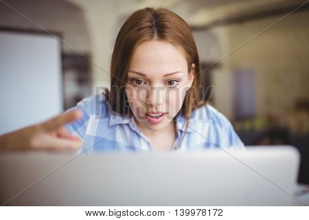 Surprised businesswoman working on laptop at desk in creative office